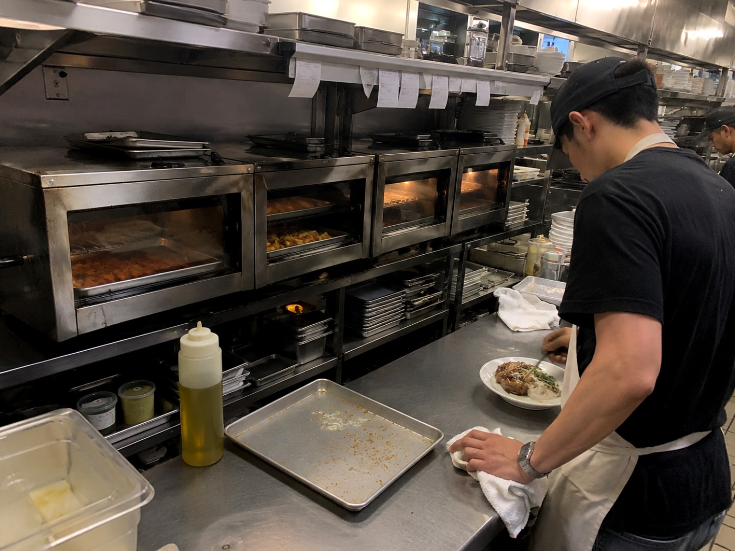 A commercial kitchen line — countertop ovens cooking unattended while a line cook plates a dish